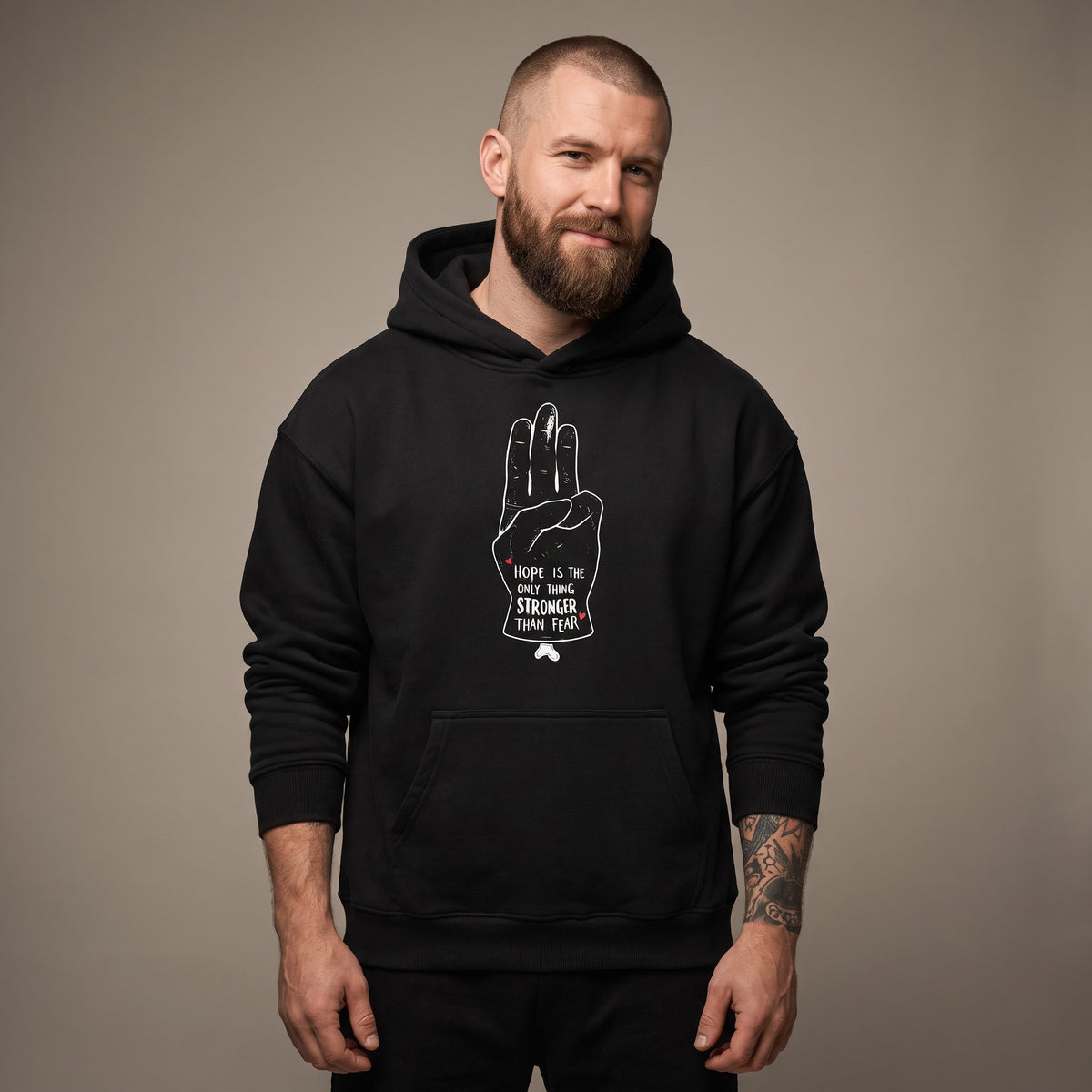 Homme portant le hoodie oversize original noir Hope, salut à trois doigts sur la poitrine, vue de face en studio