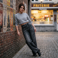 Femme portant le jean wide leg noir délavé contre un mur de briques devant une friterie