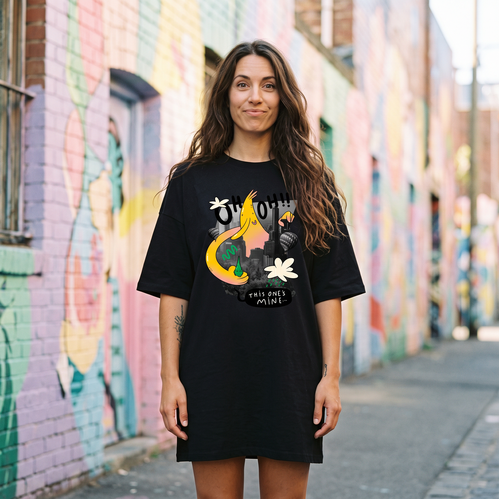 Robe t-shirt oversize noire au monstre cartoon jaune Oh Oh, portée dans une ruelle street-art colorée