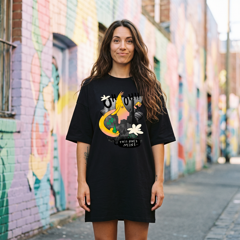 Robe t-shirt oversize noire au monstre cartoon jaune Oh Oh, portée dans une ruelle street-art colorée