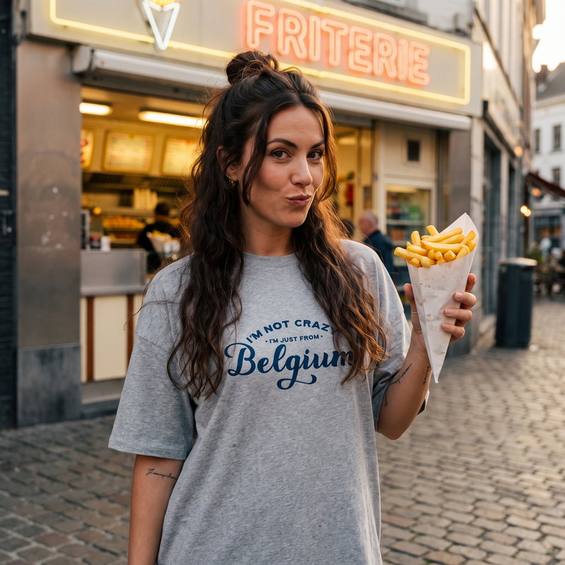 Robe t-shirt oversize grise avec inscription humoristique "I'm not crazy, I'm just from Belgium", portée devant une friterie belge illuminée