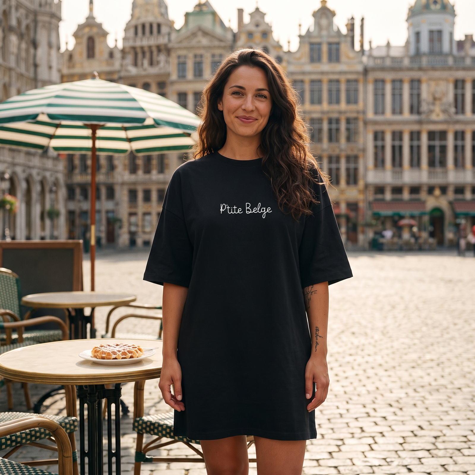 Robe t-shirt oversize noire P'tite Belge portée en terrasse sur une place pavée de Bruxelles avec une gaufre