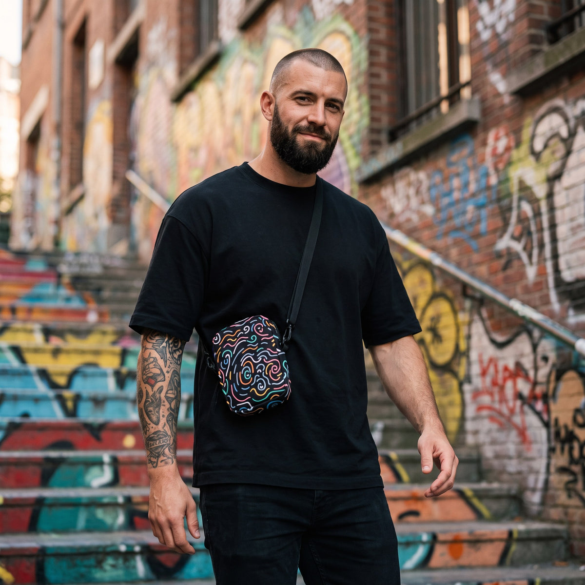 Sac bandoulière noir à gribouillis colorés porté par un homme, look streetwear en Belgique | CHT'M Boutique