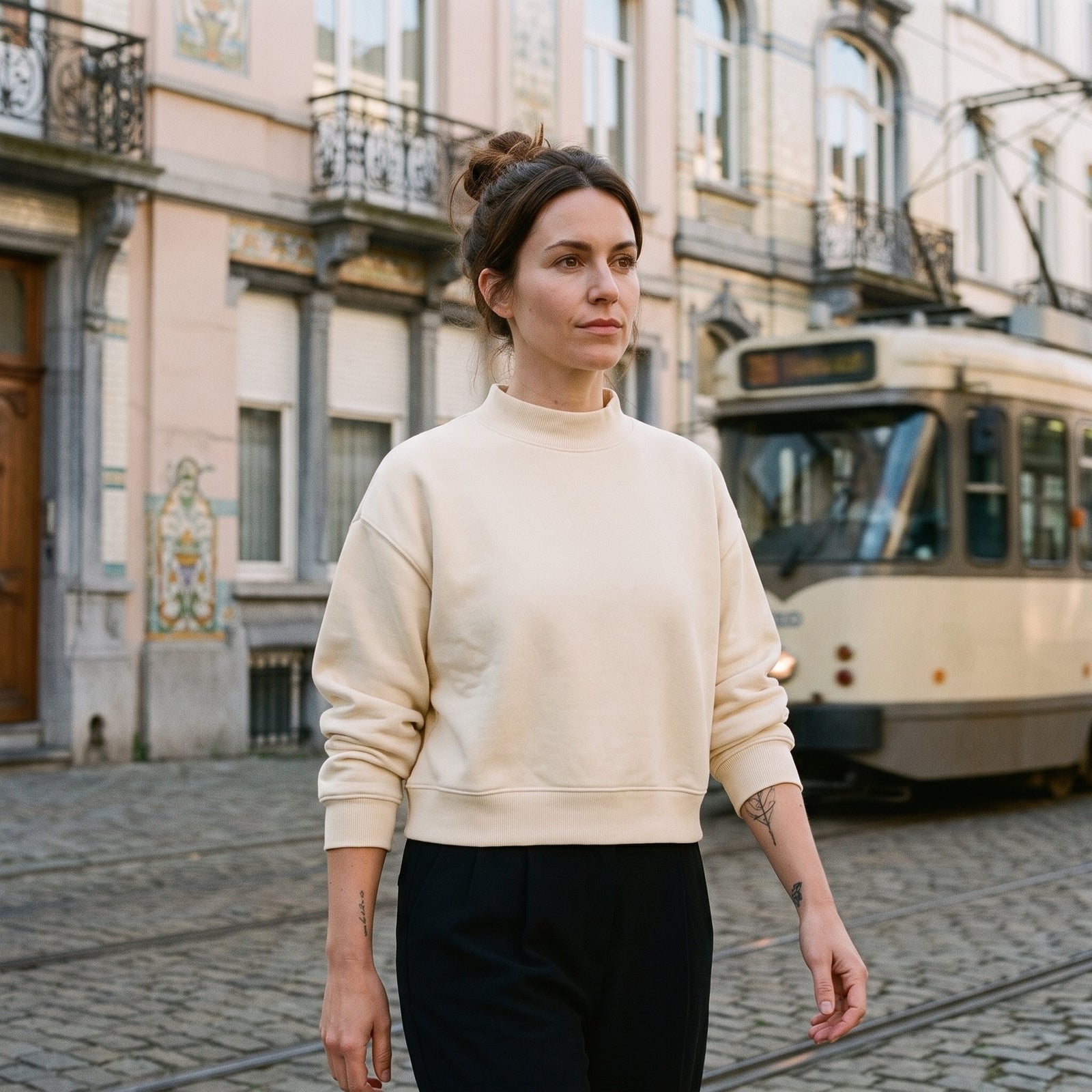 Femme portant le sweat crop col montant original CHT'M abricot crème, devant des façades Art nouveau à Bruxelles