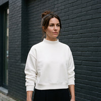 Femme portant le sweat crop col montant original CHT'M blanc, devant un mur de briques