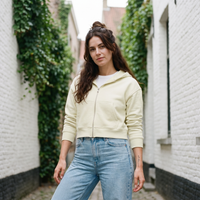Femme portant le sweat zippé crop top amande avec un jean dans une ruelle