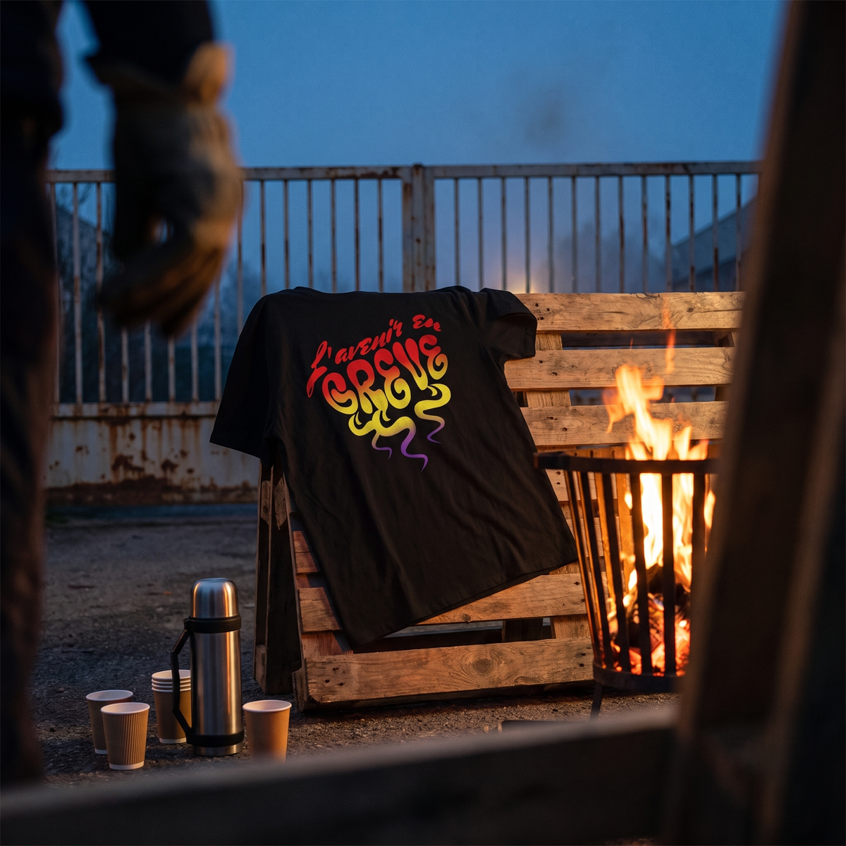 T-shirt Gen Z noir « L'avenir en grève » posé sur une palette près d'un brasero, piquet de grève à l'aube – t-shirt manif pas cher CHT'M