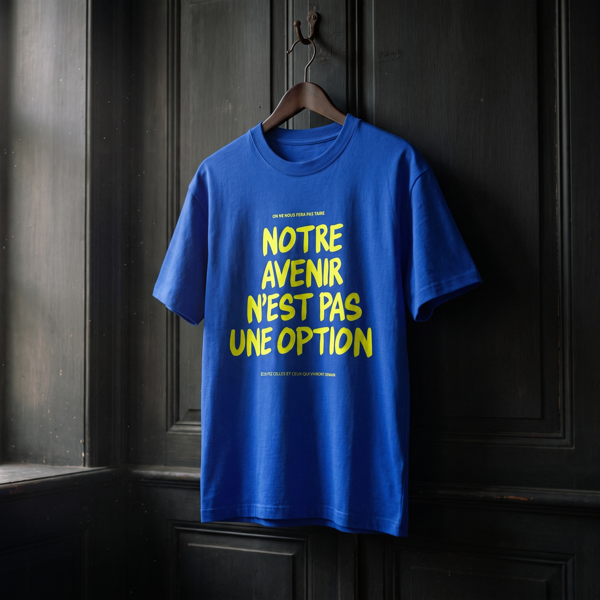 T-shirt Gen Z bleu roi « Notre avenir n'est pas une option », slogan jaune fluo, sur cintre en bois dans un intérieur sombre – t-shirt manif original CHT'M