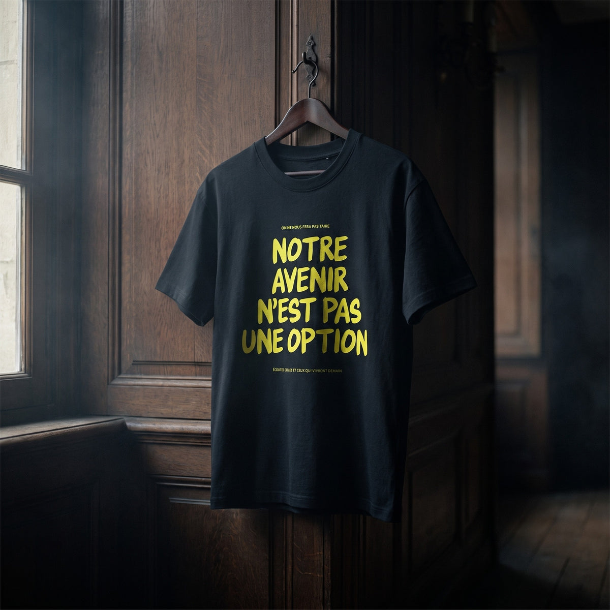 T-shirt Gen Z noir « Notre avenir n'est pas une option », slogan jaune fluo, suspendu sur un cintre en bois dans un intérieur sombre – t-shirt manif original CHT'M