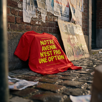 T-shirt Gen Z rouge « Notre avenir n'est pas une option » posé sur les pavés après une marche, pancarte en carton – t-shirt manif original CHT'M