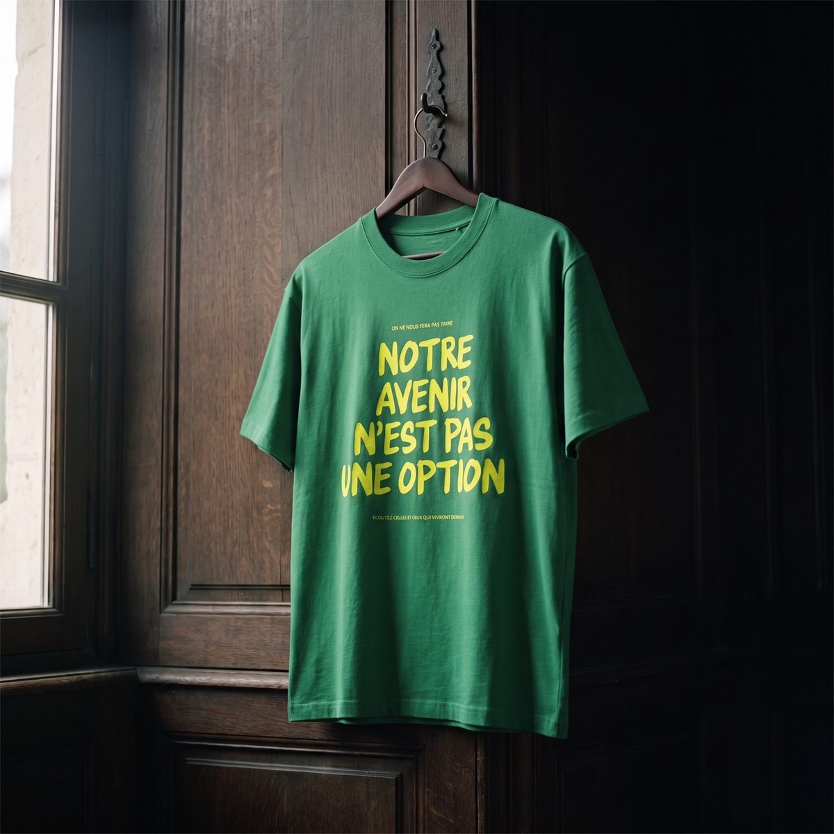 T-shirt Gen Z vert prairie « Notre avenir n'est pas une option », slogan jaune fluo, sur cintre en bois dans un intérieur sombre – t-shirt manif original CHT'M