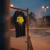 T-shirt oversized délavé Gen Z noir « Stay Strong la Gène Z » accroché au grillage d'un skatepark au crépuscule – tshirt genz pas cher CHT'M