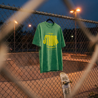 T-shirt oversized délavé Gen Z vert prairie « Stay Strong la Gène Z » accroché au grillage d'un skatepark au crépuscule – tshirt genz pas cher CHT'M