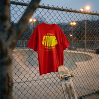 T-shirt oversized Gen Z rouge « Stay Strong la Gène Z » accroché au grillage d'un skatepark au crépuscule – tshirt genz pas cher CHT'M