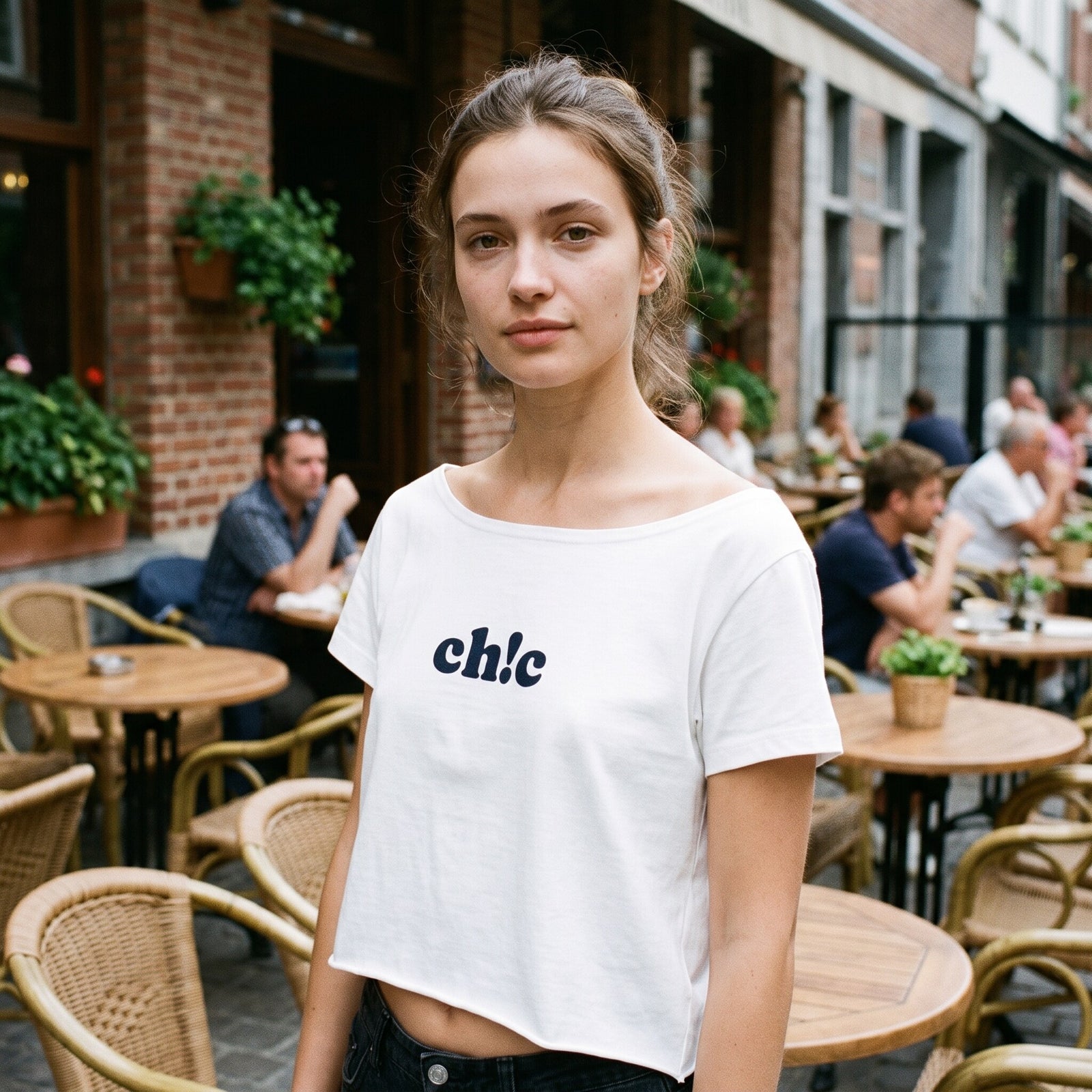 Crop top blanc epaules denudees au lettrage ch!c bleu marine, porte en terrasse d'un cafe belge en ete