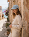 Femme portant une casquette en jean bleu clair brodée fleur, arc-en-ciel et peace, dans une ruelle méditerranéenne ensoleillée