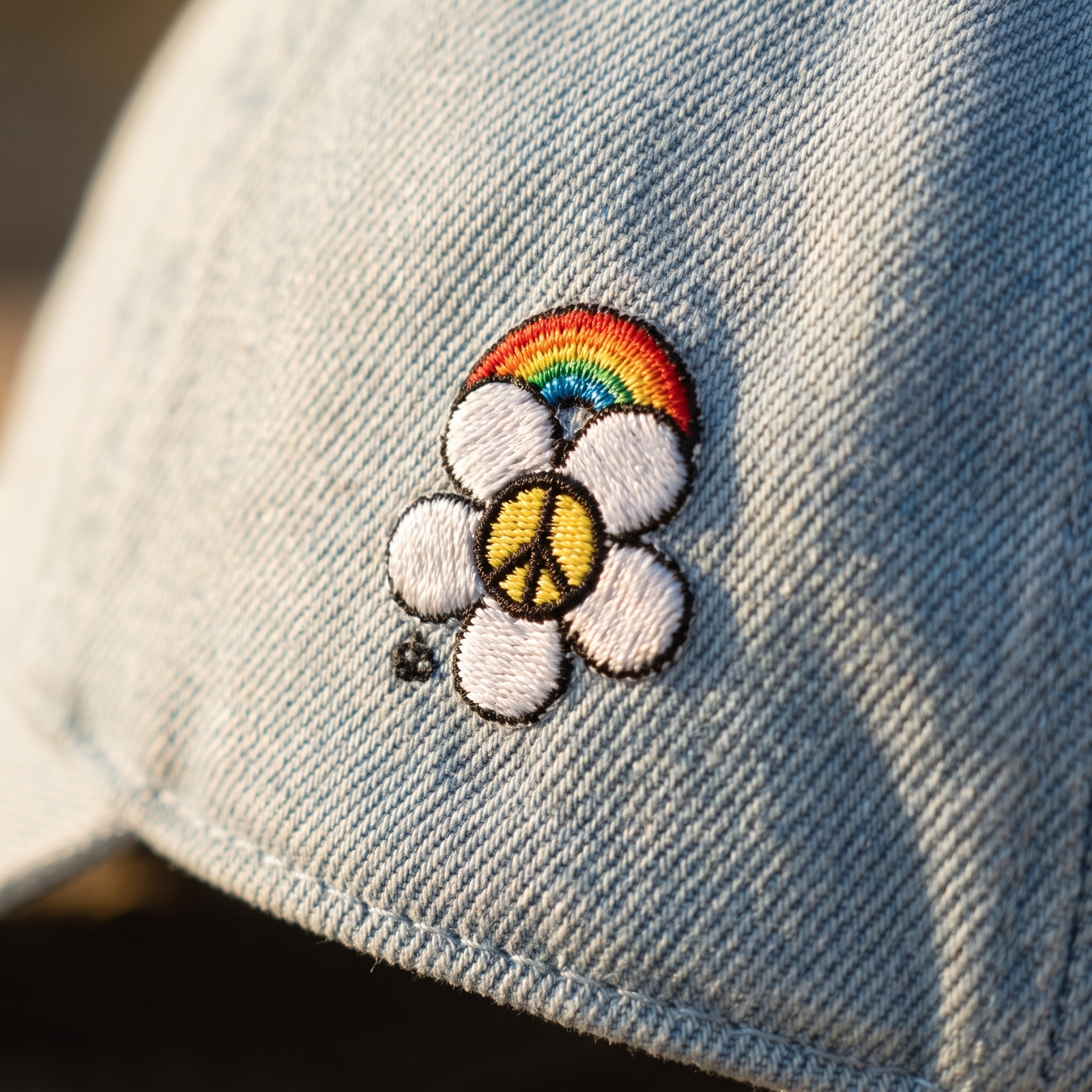 Gros plan de la broderie fleur, arc-en-ciel et symbole peace sur casquette en jean bleu clair