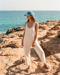 Femme portant une casquette en jean bleue brodée fleur peace au bord de la mer sur les rochers