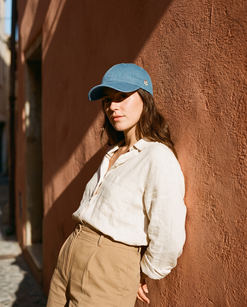 Casquette en jean bleue brodée fleur peace portée devant un mur terracotta au soleil