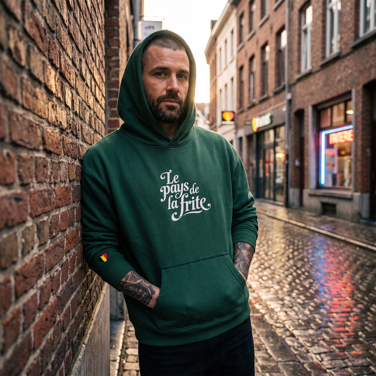 Hoodie belge original Le Pays de la Frite vert sapin porte en rue devant une friterie, streetwear belge