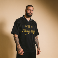 Maillot de foot streetwear Zwanze City noir porté par un homme en studio, buzz cut, barbe et tatouages
