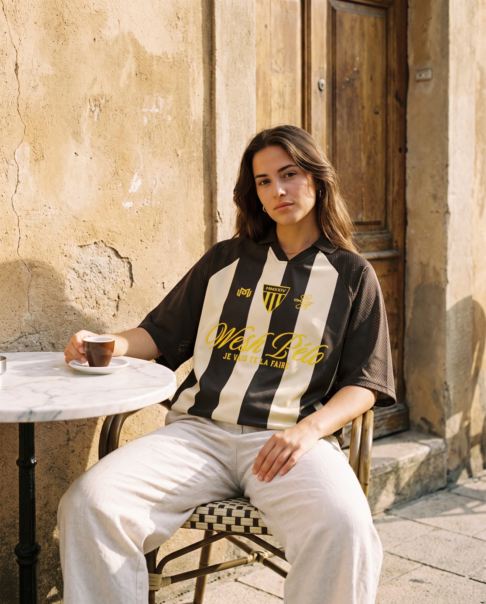 Femme portant le maillot de foot oversize Wesh Pélo coloris Café Abricot en terrasse de café méditerranéen
