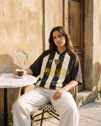 Femme portant le maillot de foot oversize Wesh Pélo coloris Café Abricot en terrasse de café méditerranéen