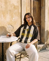 Femme portant le maillot de foot oversize Wesh Pélo coloris Café Abricot en terrasse de café méditerranéen