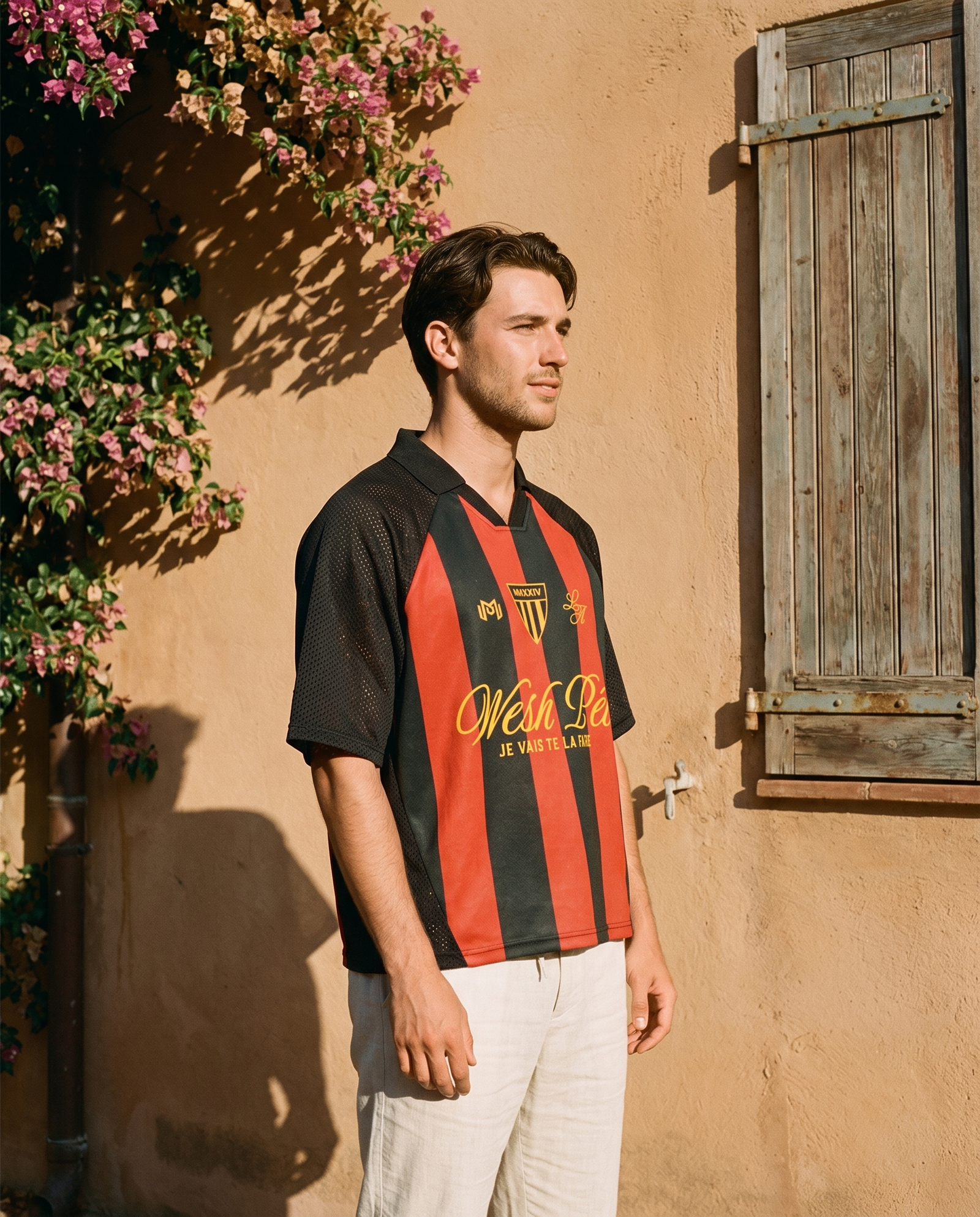 Homme de profil portant le maillot de foot Wesh Pélo Noir & Rouge contre un mur ocre méditerranéen – streetwear CHT'M