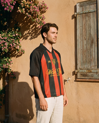 Homme de profil portant le maillot de foot Wesh Pélo Noir & Rouge contre un mur ocre méditerranéen – streetwear CHT'M