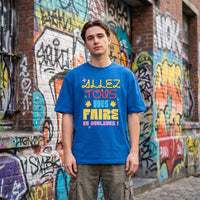T-shirt oversized bleu vif Allez tous vous faire en couleurs, porté devant un mur de graffitis dans une ruelle pavée