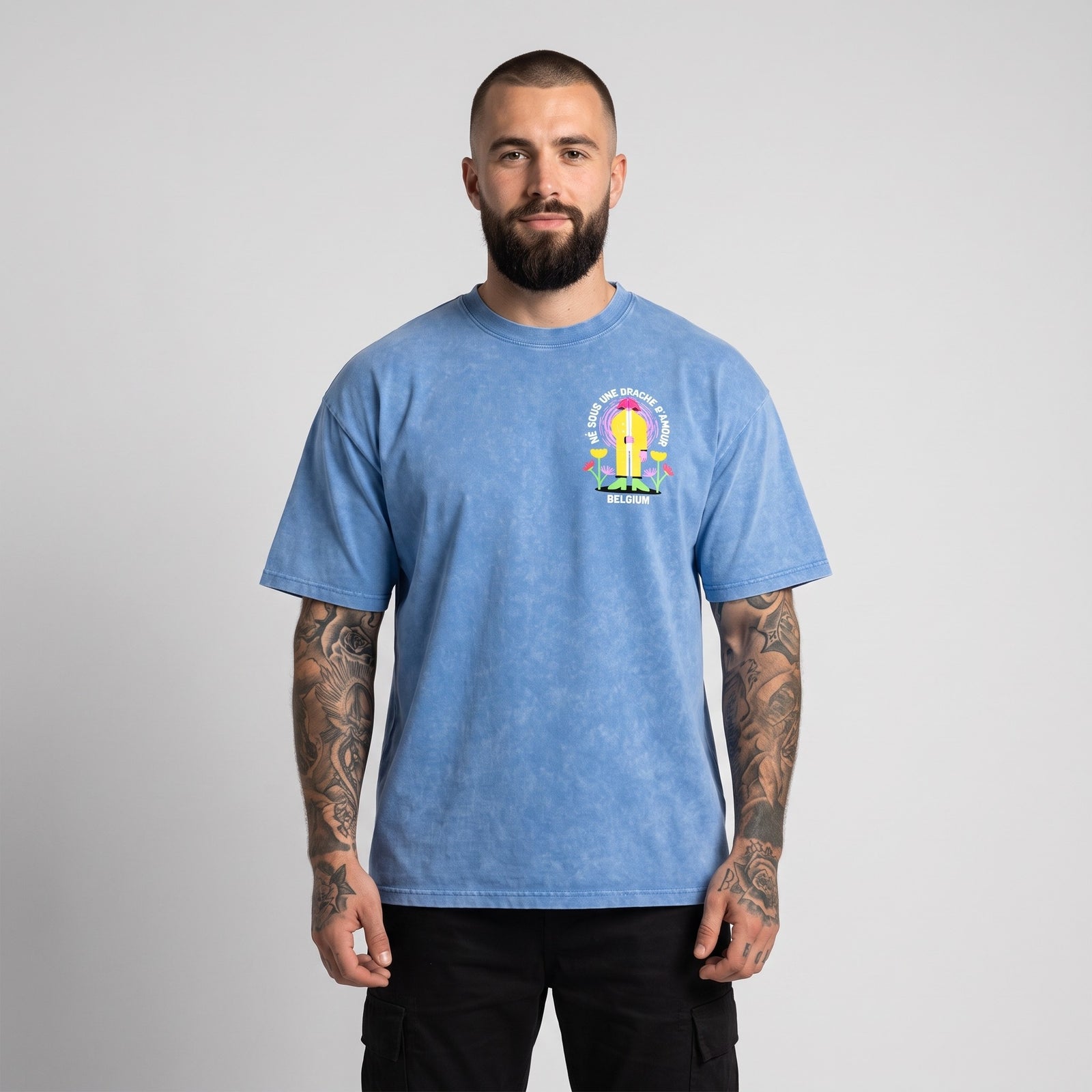 Homme barbu et tatoué en studio portant de face le t-shirt belge oversized bleu délavé drache d'amour
