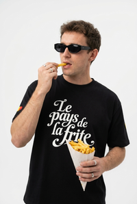 Homme portant le t-shirt belge oversized noir Le Pays de la Frite, cône de frites en main