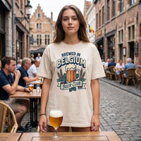 Femme en terrasse d'une ruelle pavée belge, t-shirt écru Brewed in Belgium Beer Club et verre de bière posé sur la table