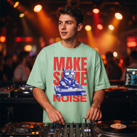 T-shirt oversized vert menthe Make Some Noise au chat DJ, porté derrière des platines dans un club éclairé