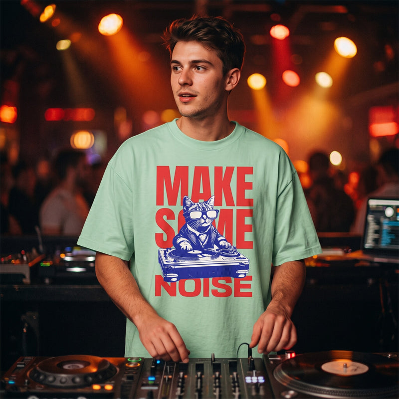 T-shirt oversized vert menthe Make Some Noise au chat DJ, porté derrière des platines dans un club éclairé