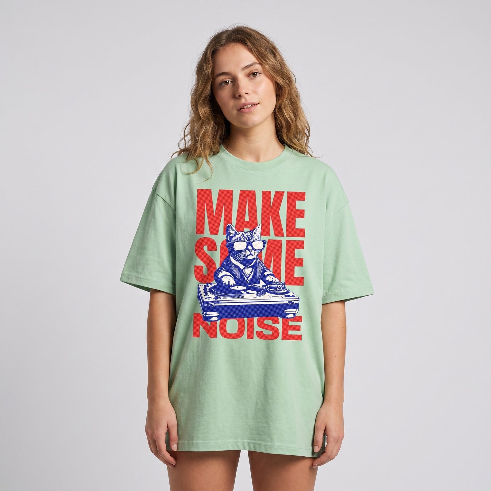 T-shirt oversized vert clair au chat DJ Make Some Noise, porté par une femme en studio sur fond gris clair
