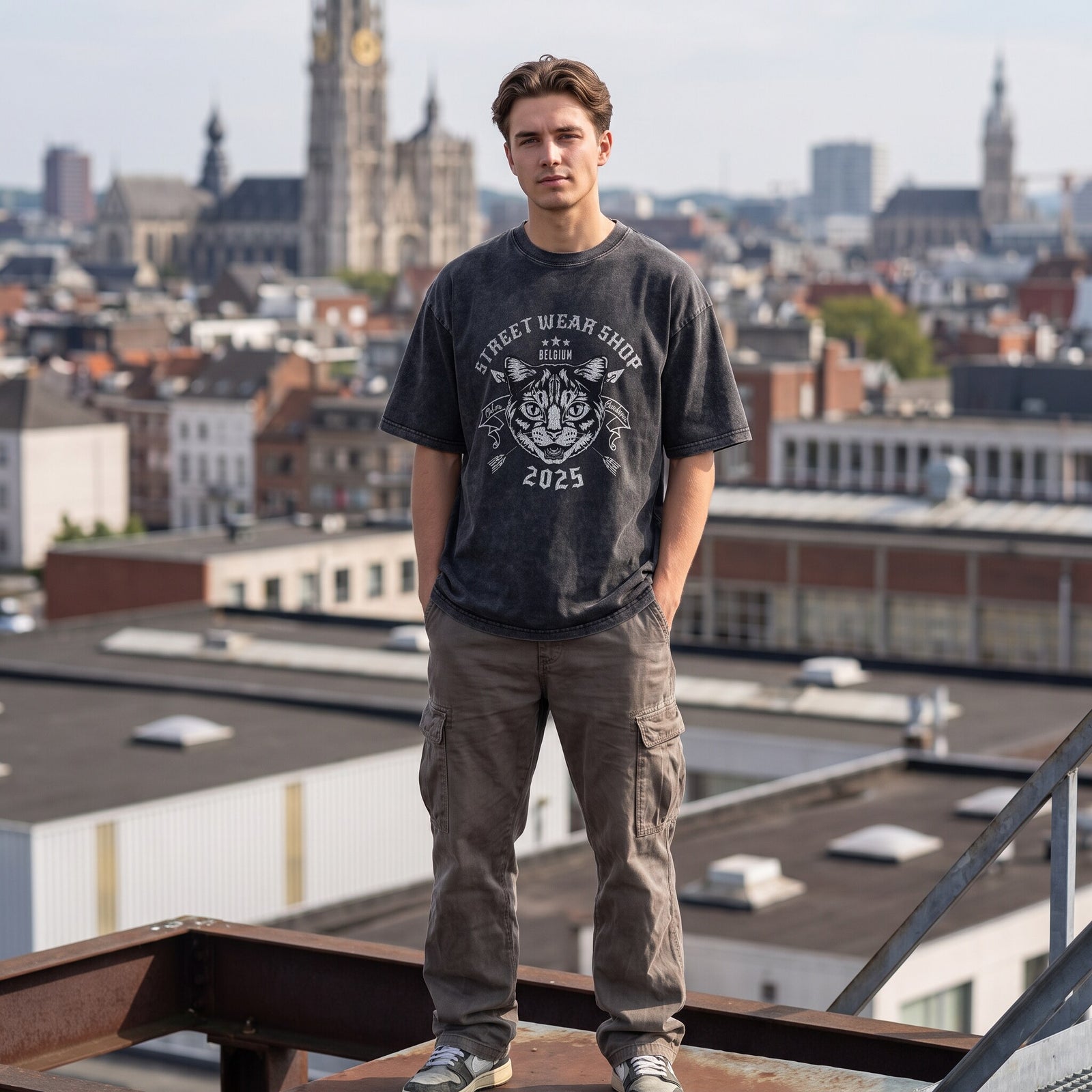 T-shirt oversized noir lavé à tête de chat blanche, plein pied sur une poutre avec les toits d'Anvers derrière