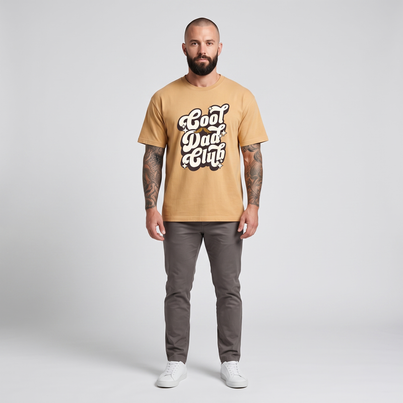 Homme barbu tatoué portant le t-shirt Cool Dad Club beige camel - photo studio