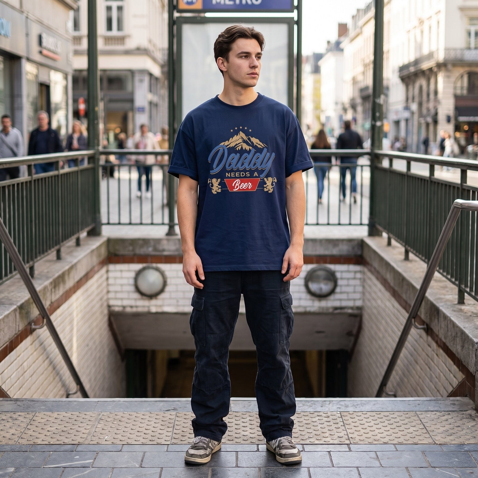 T-shirt oversized papa bière bleu marine, montagne dorée et bandeau rouge, devant une bouche de métro bruxelloise