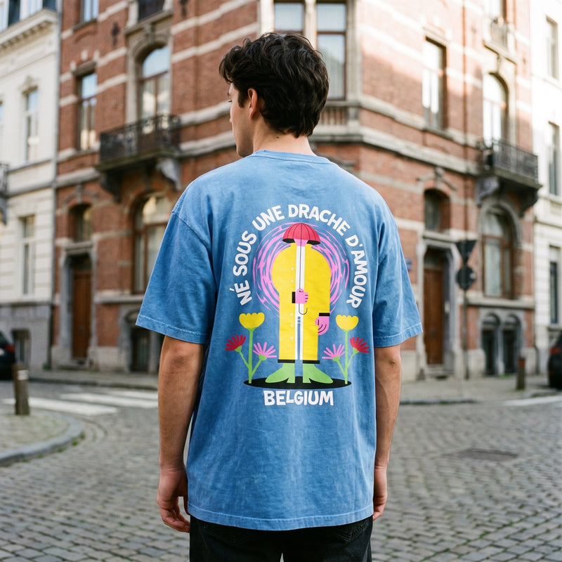 Homme de dos en t-shirt bleu snow wash Né sous une drache d'amour, à un coin de rue bruxellois aux façades de brique