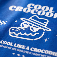 Gros plan sur l'impression blanche du crocodile à lunettes et chapeau, sur le coton bleu vif d'un t-shirt enfant