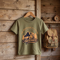 T-shirt enfant kaki montagne vintage sur cintre en bois, accroche a un mur de planches pres d'un sac a dos