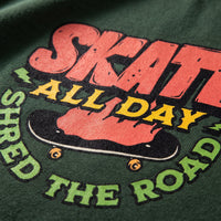 Detail du skateboard et du slogan Shred the Road imprimes en vert et rouge sur le coton vert fonce