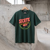 T-shirt enfant vert fonce Skate All Day sur cintre, pose contre un bloc de beton dans un skatepark