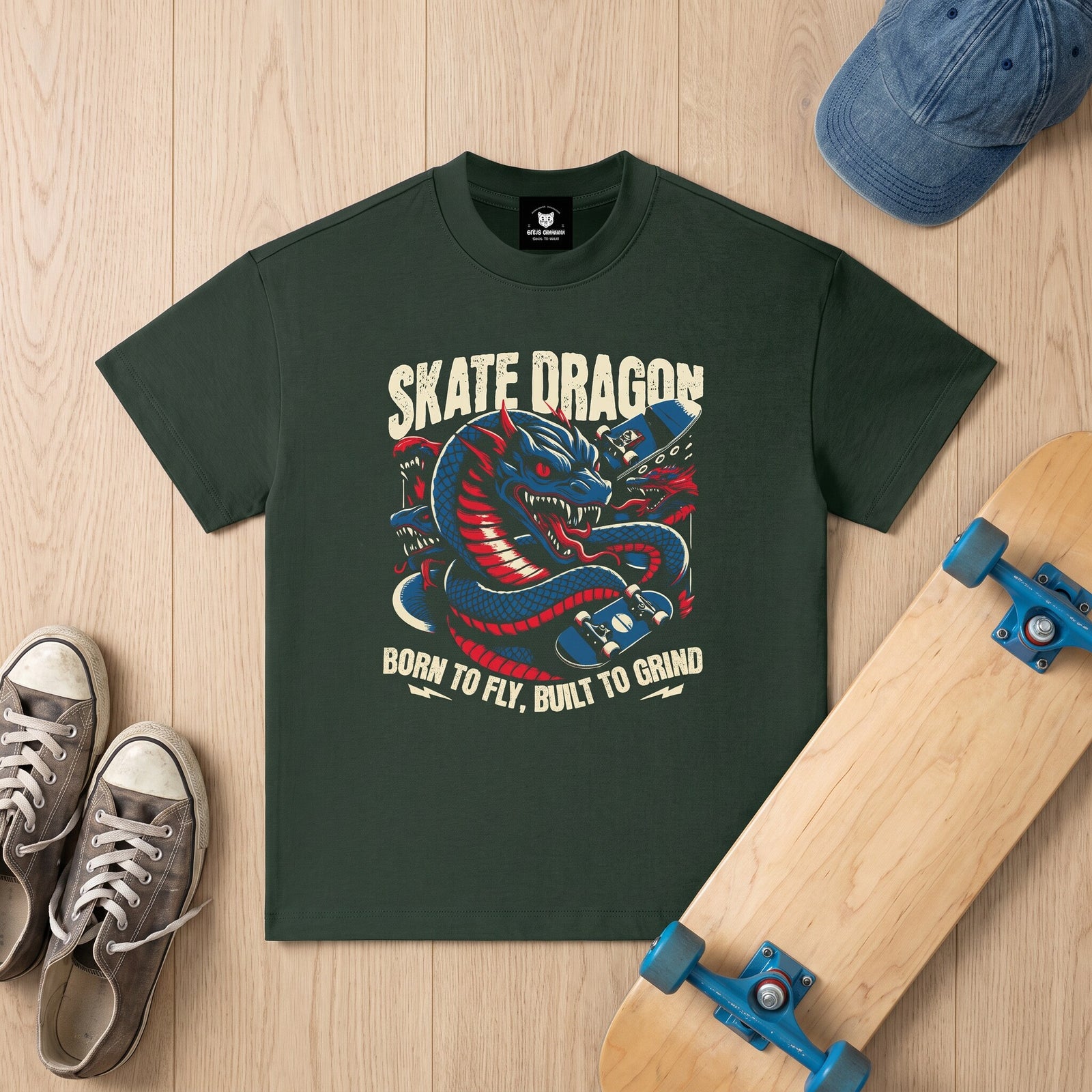 T-shirt vert sapin imprime dragon bleu et rouge, pose a plat avec une casquette en jean et un skate en erable
