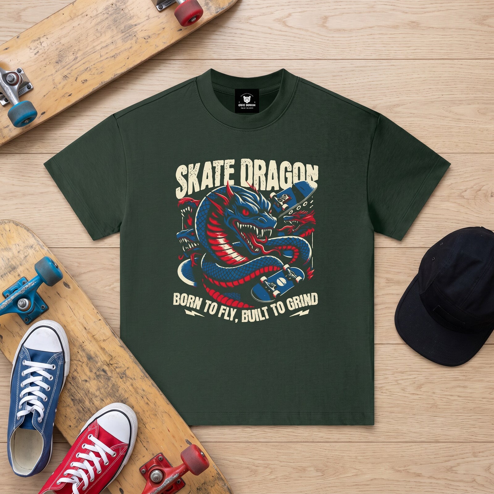 T-shirt enfant vert fonce Skate Dragon a plat sur un parquet clair, entre deux skateboards et des Converse colorees