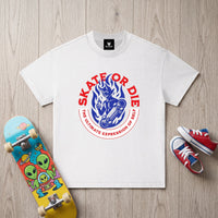 T-shirt enfant blanc au demon skateur, pose a plat pres d'un skateboard colore et de baskets rouges