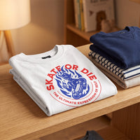T-shirt enfant blanc Skate or Die plie sur une etagere en bois, pres d'une lampe et de pulls empiles