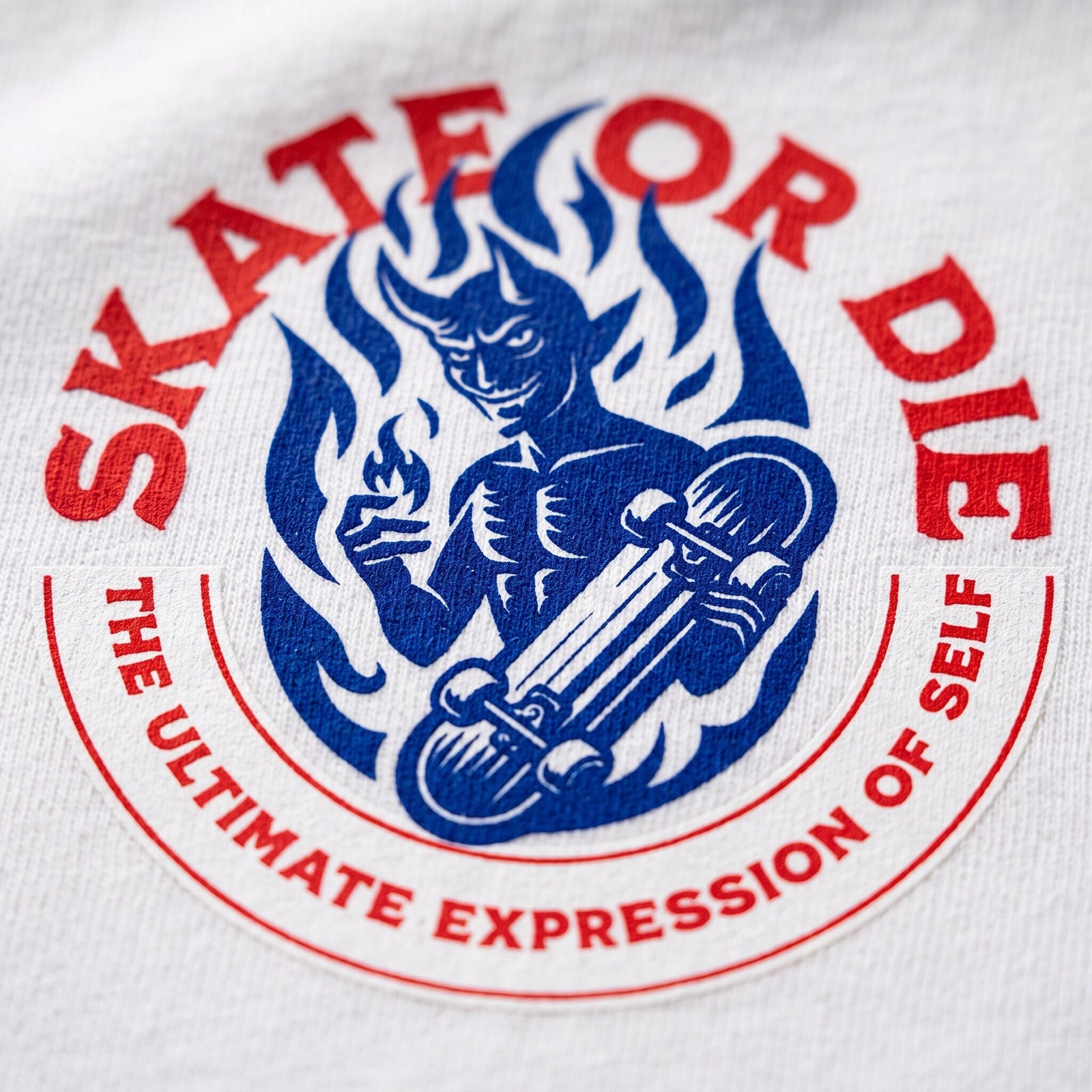 Gros plan sur le demon skateur bleu en flammes et le lettrage rouge Skate or Die imprimes sur coton blanc